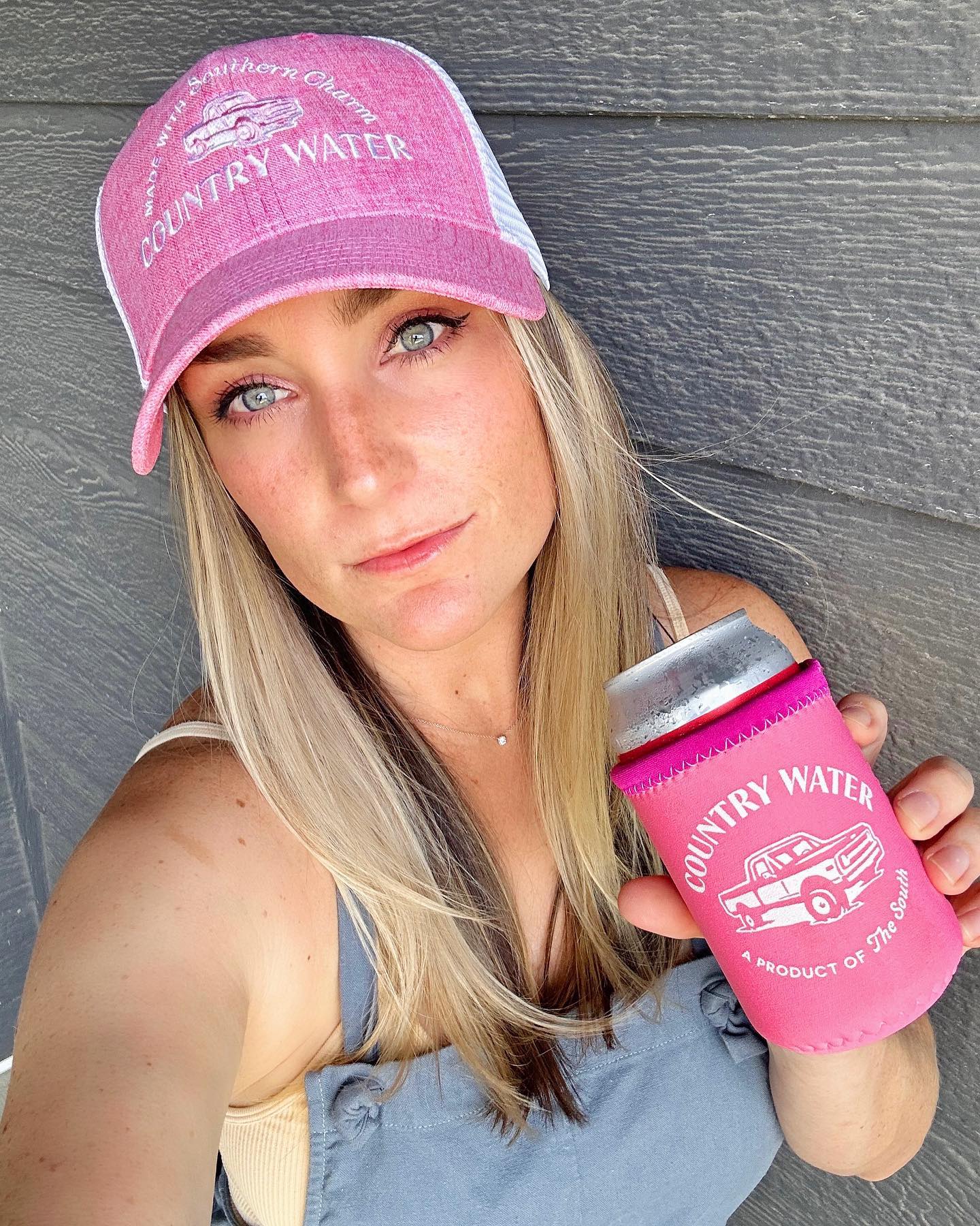 Country Water: Barbie Edition. Woman in pink hat, holding up a pink can of Country Water for a selfie
